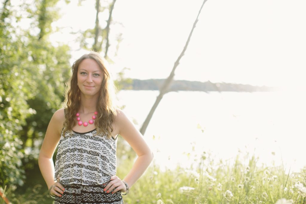 girl in tank top stands with hands on hip and backlit by sun by Prairie Creek Reservoir in Muncie senior portraits