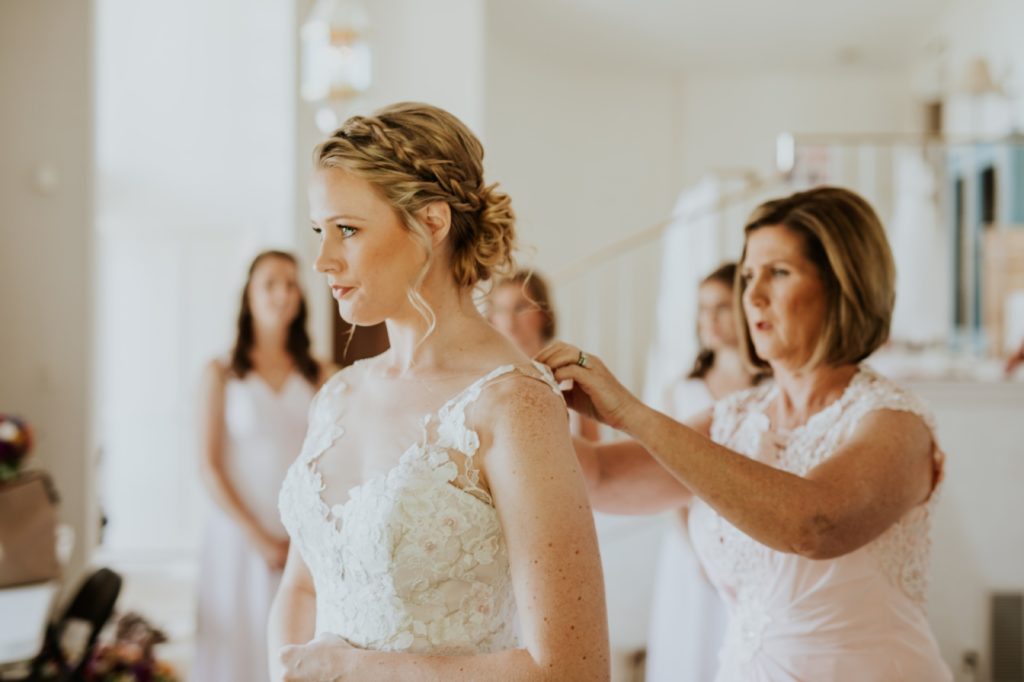 mother of bride helps bride into wedding dress for her muncie wedding photography