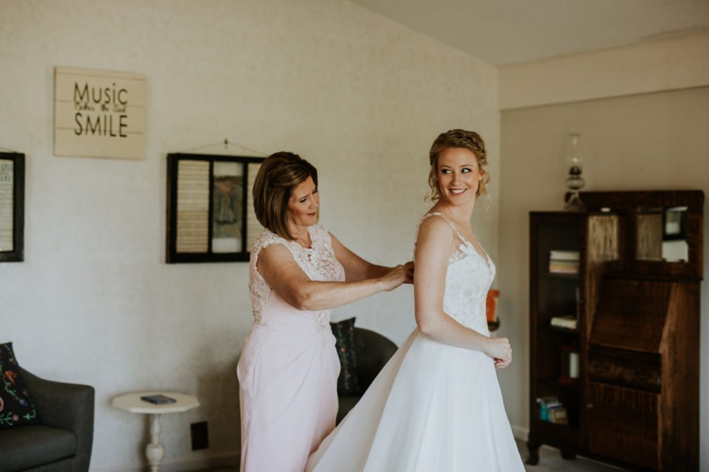 mother of bride helps blonde bride into wedding dress for her muncie wedding photography