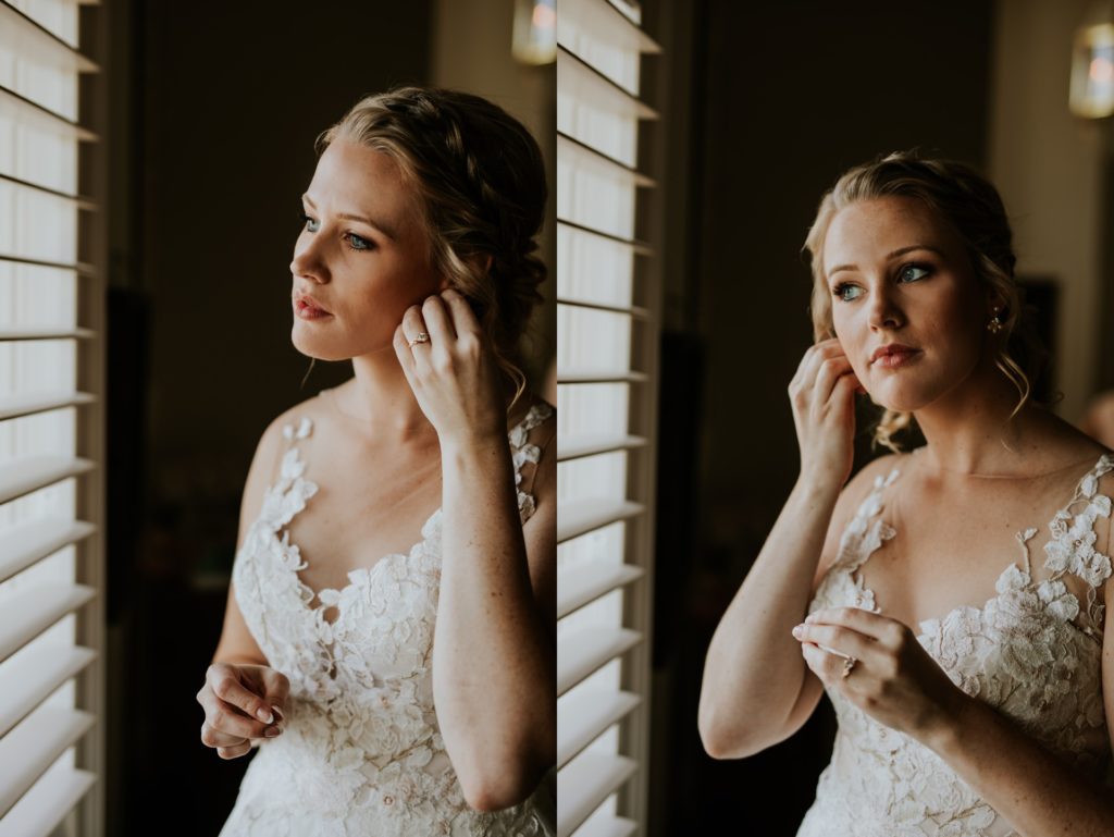 bride stands next to window and puts earrings in ears