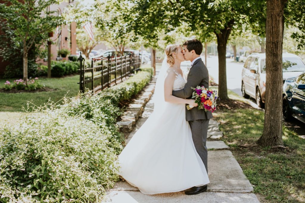 bride and groom kiss on sidewalk under trees during their muncie wedding photography