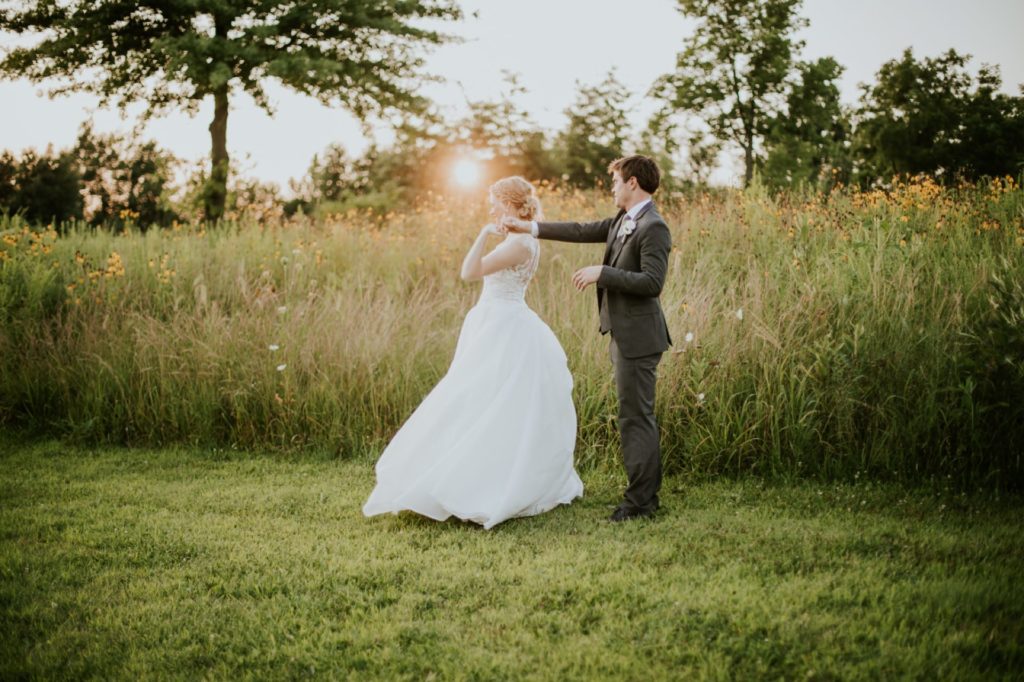groom spins bride in front of field of long grass for their muncie wedding photography