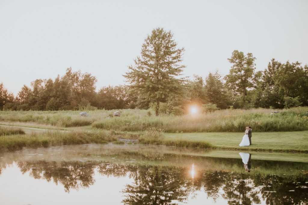 sun sets behind bride and groom in front of field next to pond for their muncie wedding photography