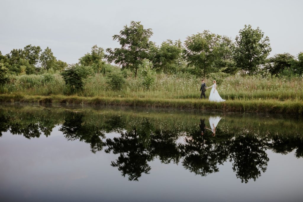 bride and groom walk along a pond during their muncie wedding photography