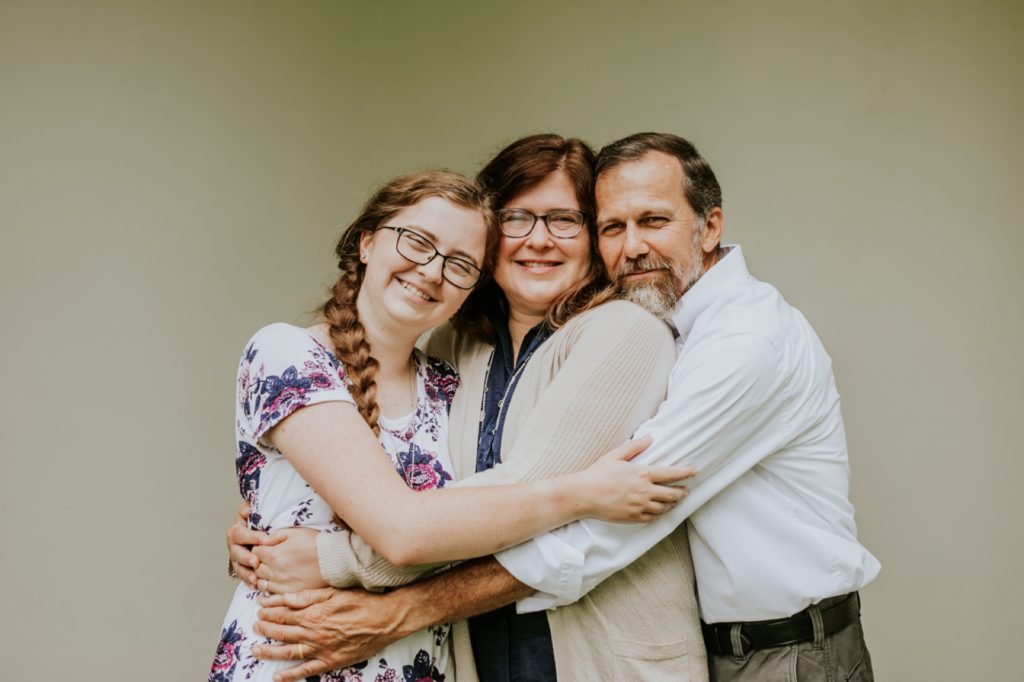 mom and dad hug their daughter under an arch