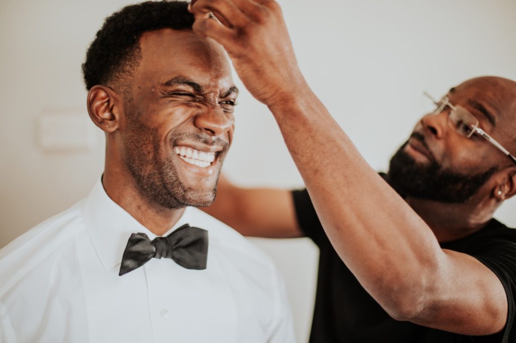 groom's dad fixes groom's hair in front of white wall at airbnb in indianapolis