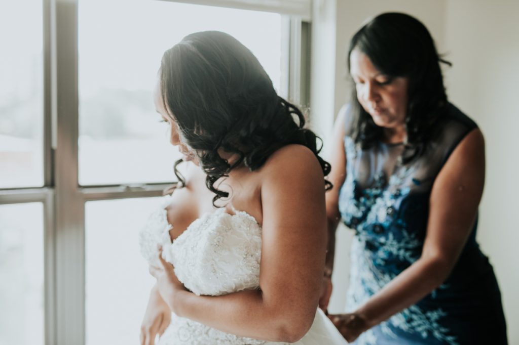 mother of bride helps bride into dress in the alexander hotel in indianapolis