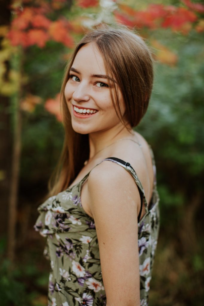 brunette girl in floral tank top smiles and looks over her shoulder in autumn in Fishers Senior Portraits