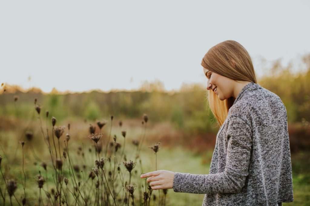 brunette girl in gray sweater walks through field at sunset in Westfield senior portraits