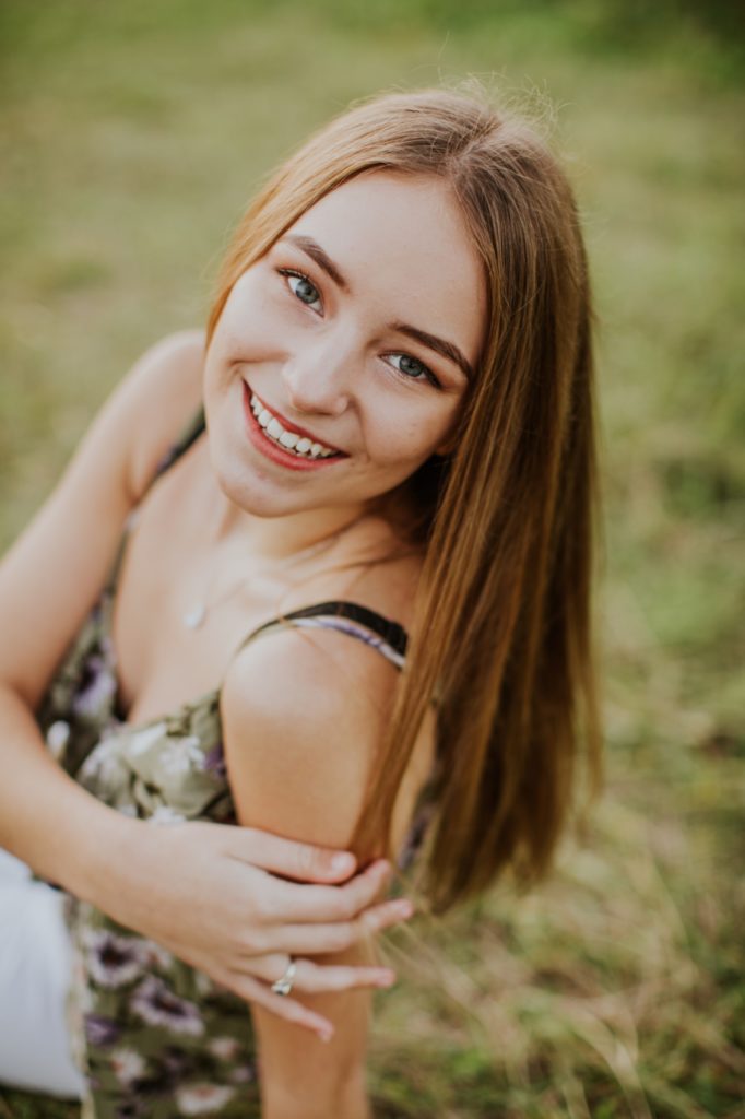 brunette girl in floral tank top smiles and looks at camera in zionsville senior portraits