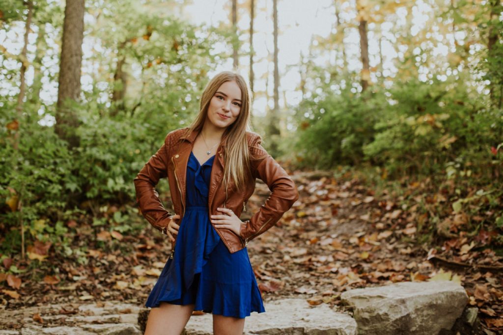 girl in brown leather jacket with blue dress in forest for Noblesville Senior Portraits