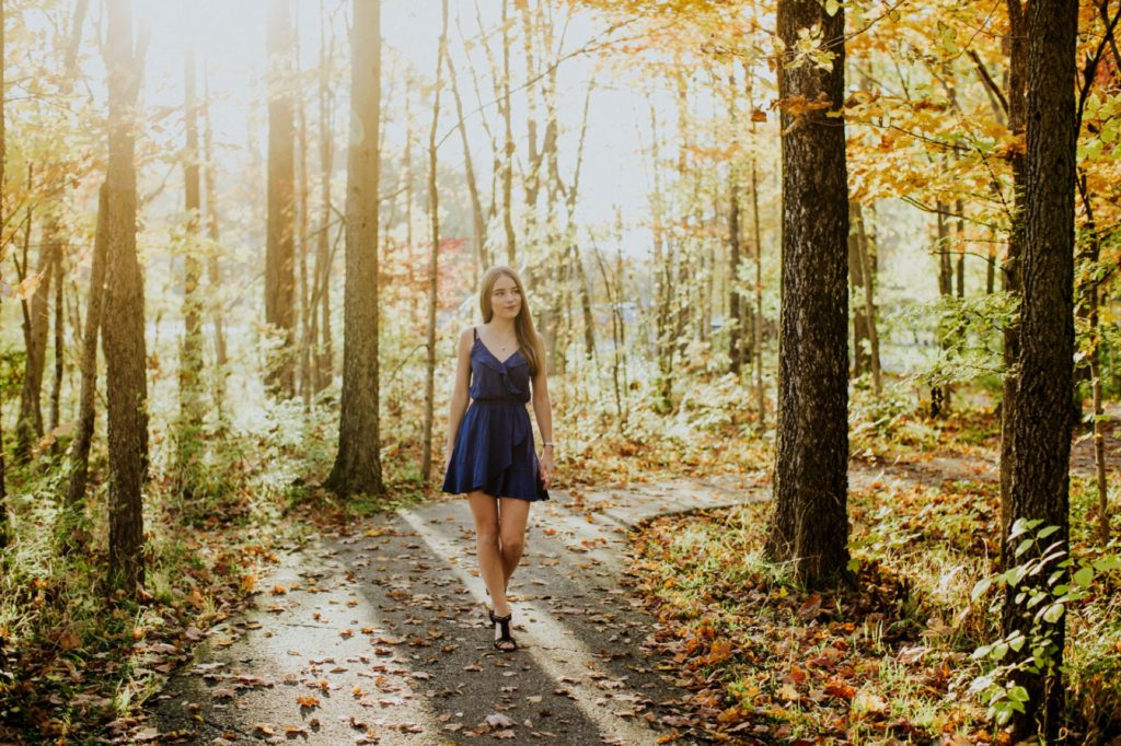 girl in blue dress walks alone in woods at sunset for Noblesville Senior Portraits