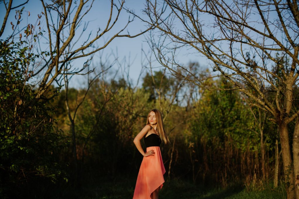 girl in pink dress in woods for dark and moody photo for Noblesville Senior Portraits
