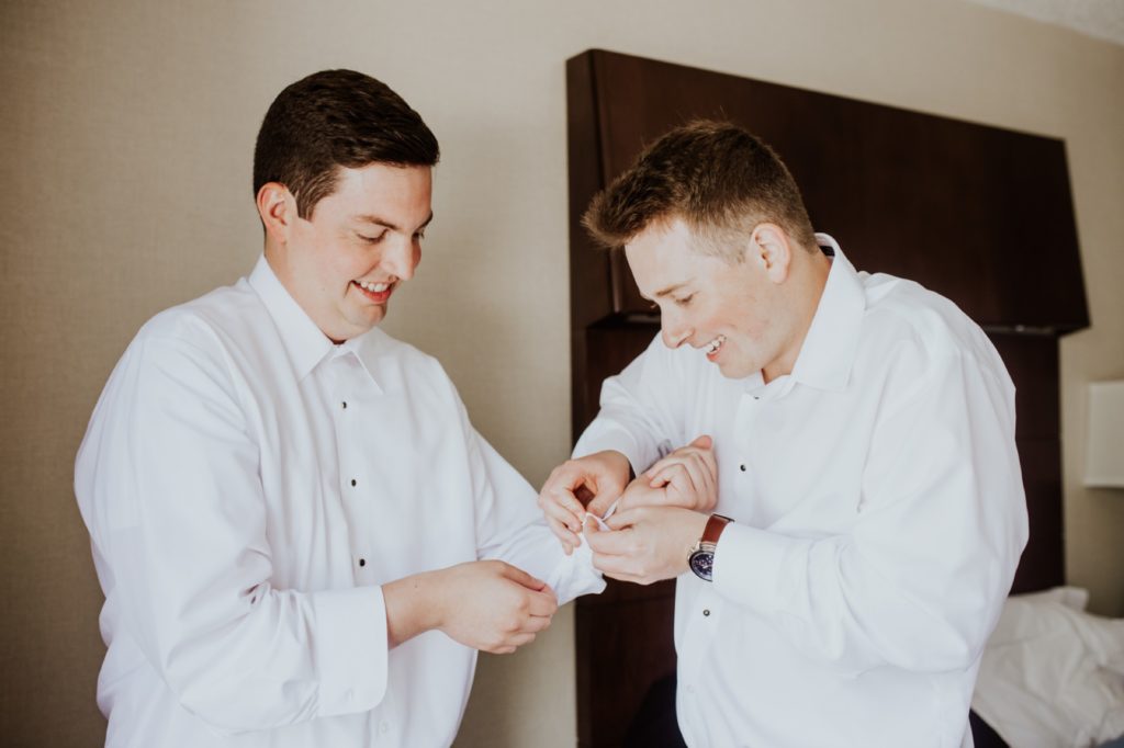 a man in a white shirt helps another man in a white shirt with his cufflinks
