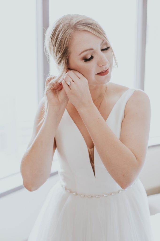 blonde bride puts earrings into her ears for a Tinker House Wedding