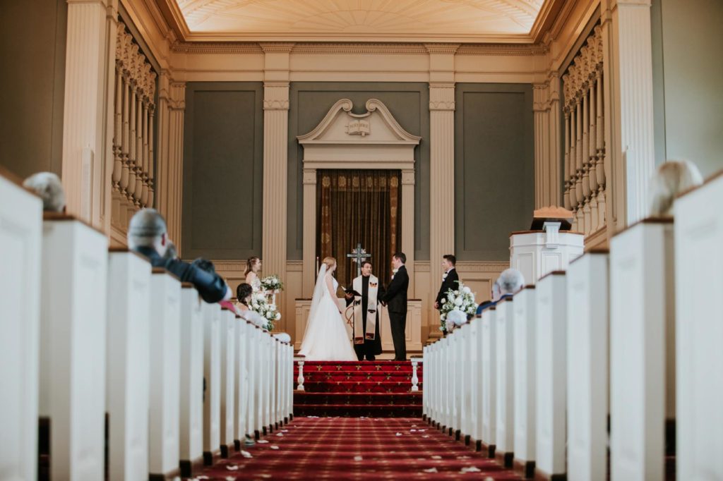 wide shot down the aisle of bride and groom exchanging vows at meridian street united methodist church