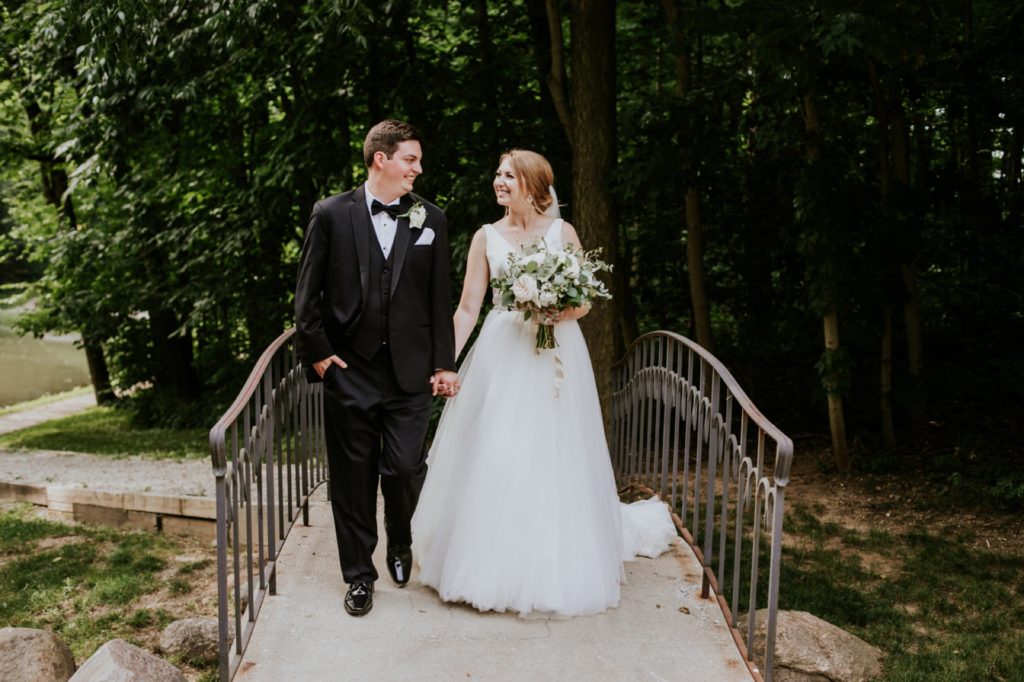 bride and groom walk across a cement bridge while bride holds flowers before their Tinker House Wedding