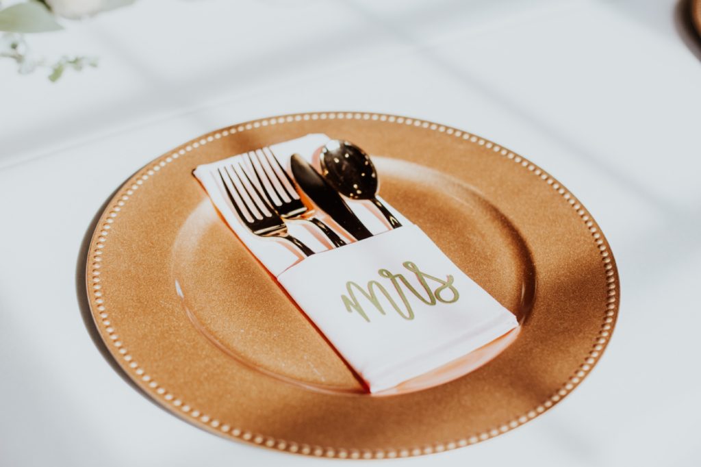 gold charger plate with napkin and gold silverware and gold "Mrs" on it at a Tinker House Wedding