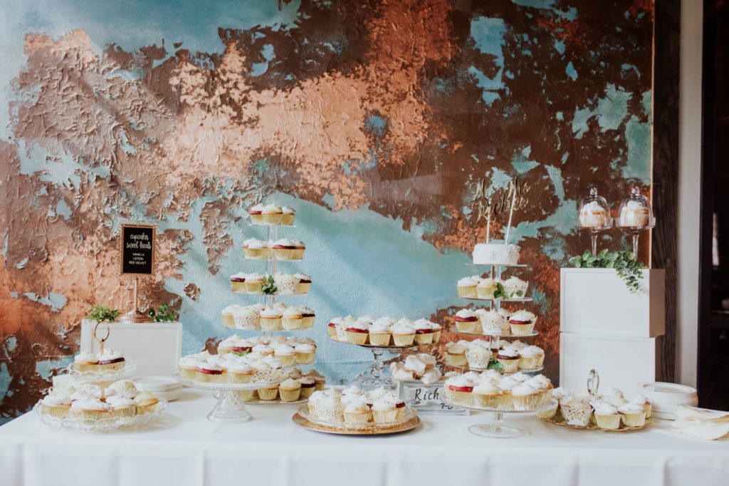 cakes and desserts in front of a dilapidated wall at a Tinker House Wedding