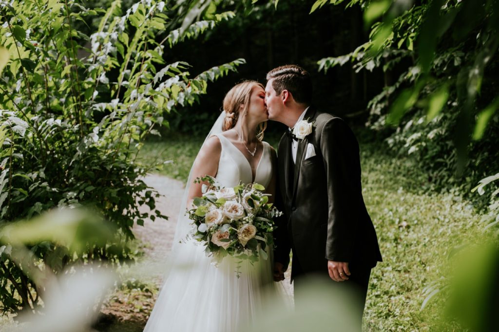 bride and groom framed by tree leaves and kissing at holcomb gardens at butler university for a Tinker House Wedding