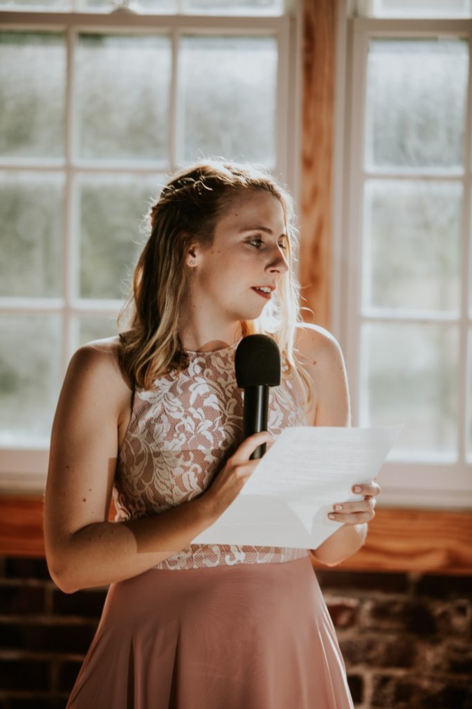 blonde maid of honor gives a speech in front of windows at a Tinker House Wedding