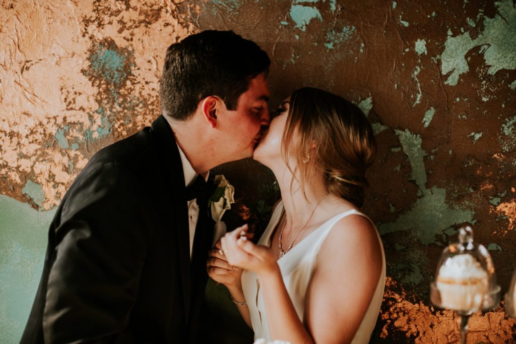 bride and groom kiss in front of dilapidated wall after having cake at their Tinker House Wedding