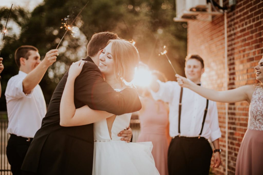 bride and groom hug at sunset while sparklers are held on all sides of them at a Tinker House Wedding