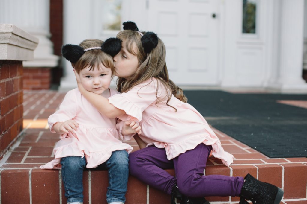 two small girls in wolf ears sit on brick and older sister kisses younger sister on head Muncie Family Photography