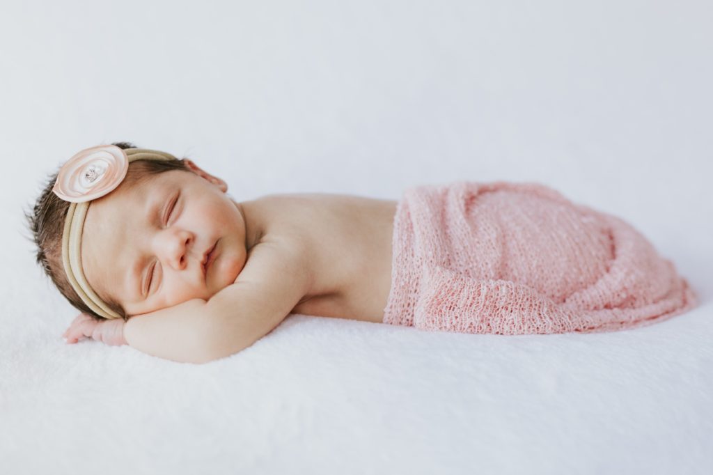 adorable baby with pink blanket covering butt and bow in hair sleeping on white blanket Noblesville Newborn Photography