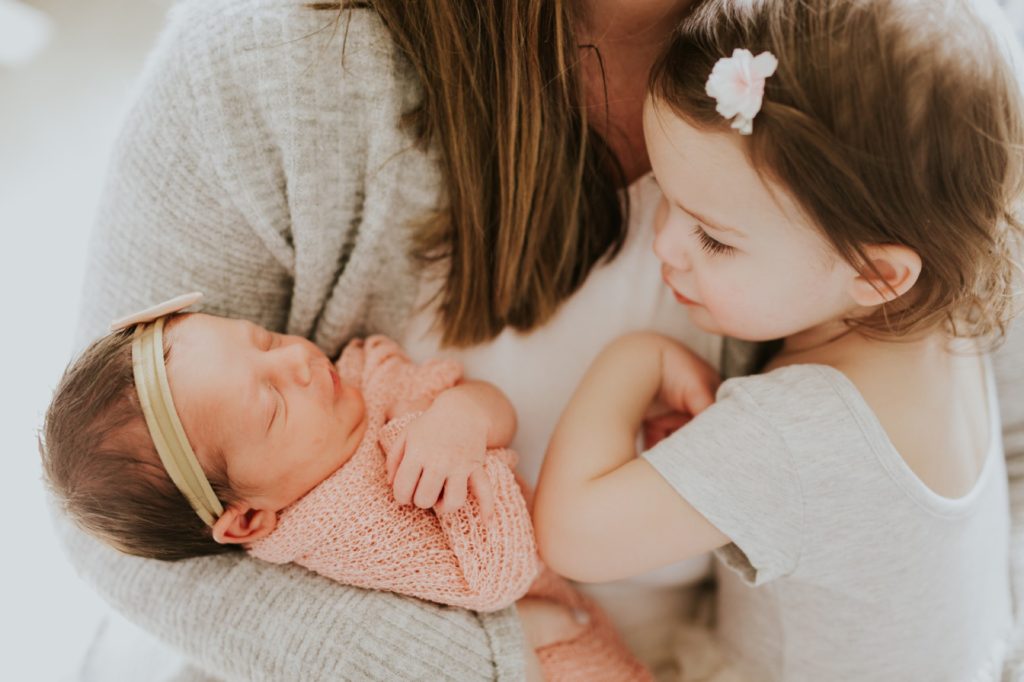 mom holds newborn baby girl and older sister in Zionsville family portraits