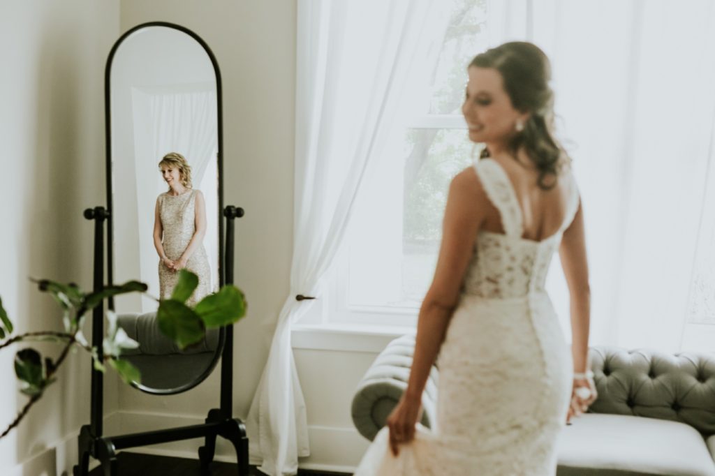 mom's reflection caught in mirror as she looks at her daughter in her wedding dress at mustard seed gardens for Noblesville Wedding Photography