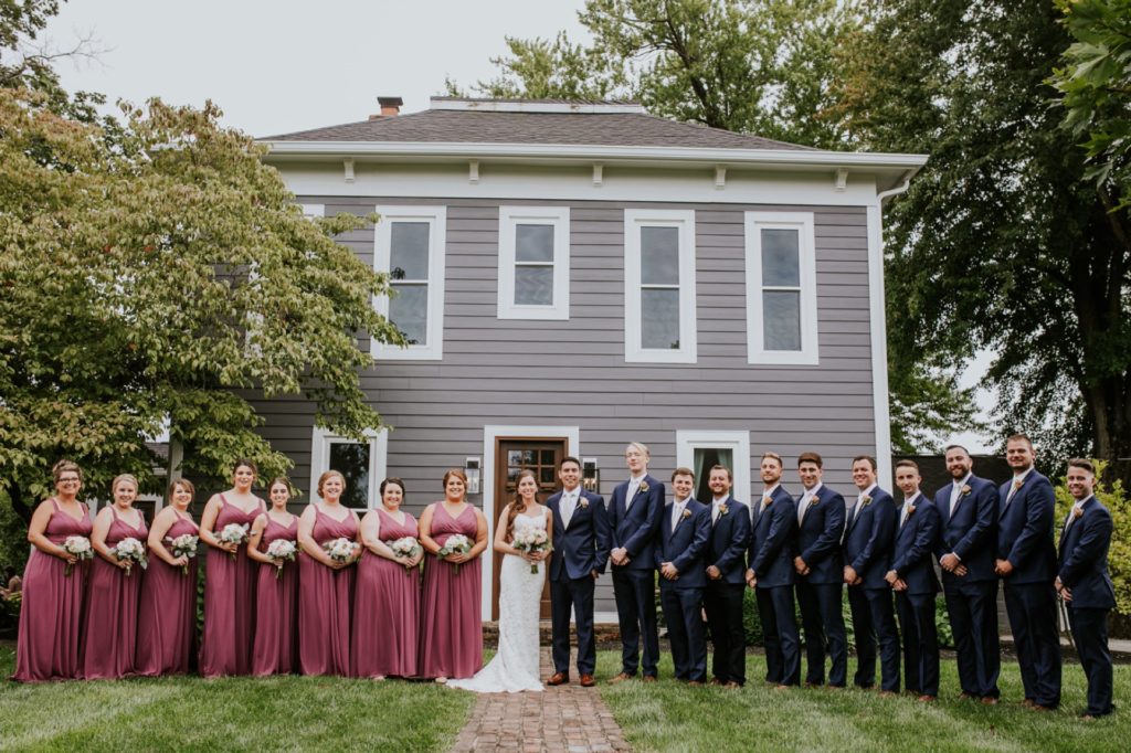 large bridal party in line in front of house at mustard seed gardens