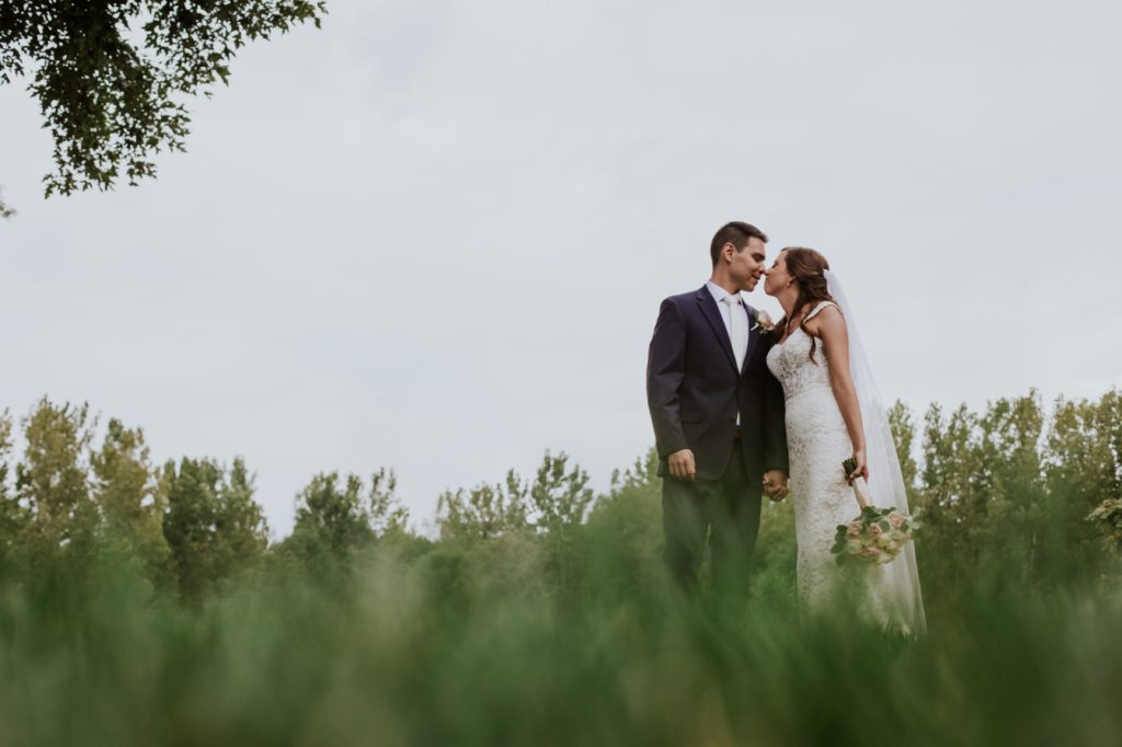 blurry grass in the foreground frames the bride and groom as they kiss at this Noblesville Wedding Photography