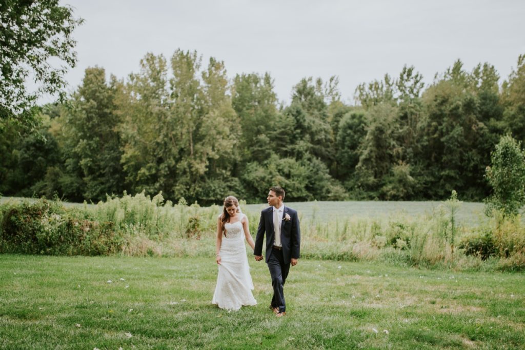 bride and groom hold hands and walk across a grassy field