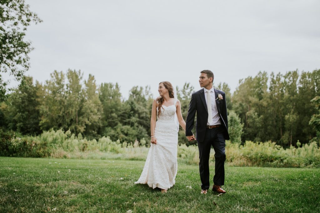 bride and groom hold hands and walk in front of a tree line