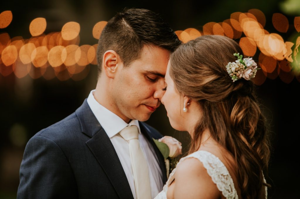 bride and groom touch foreheads in front of bokeh from string lights for Noblesville Wedding Photography