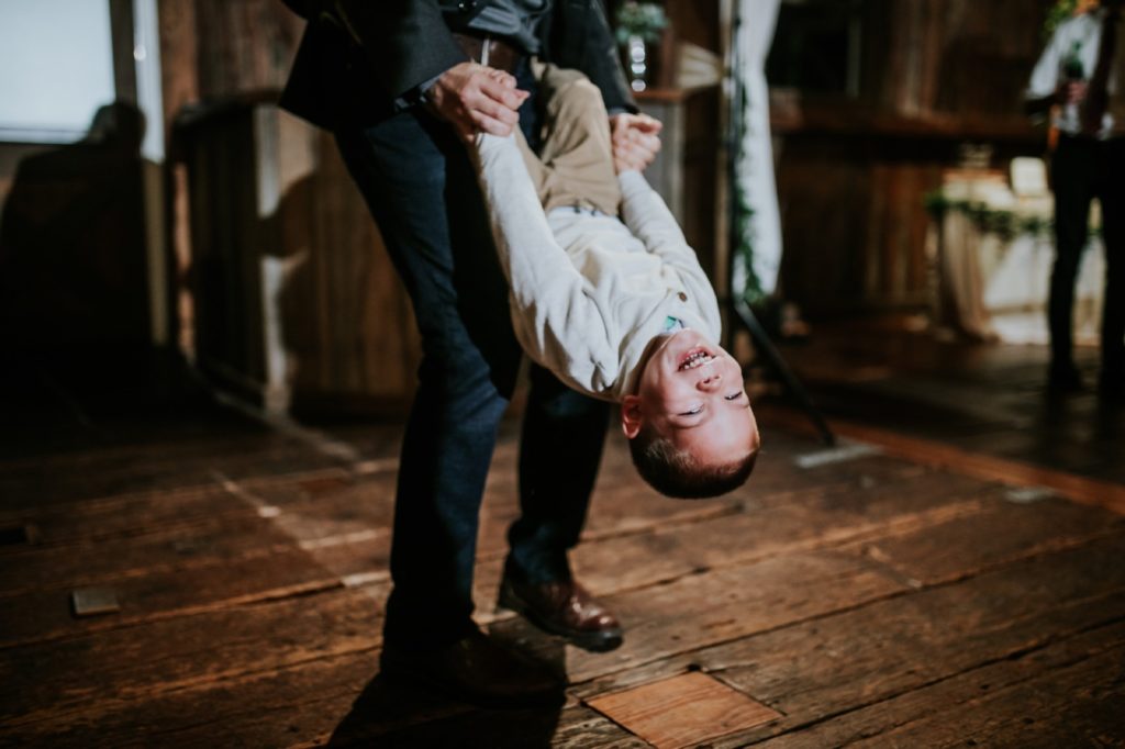 young boy flips upside down while holding dad's hands at mustard seed gardens for Noblesville Wedding Photography