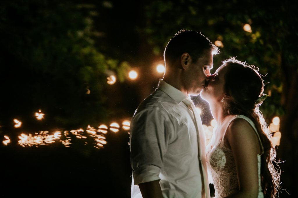 bride and groom kiss outside at night in front of string lights at mustard seed gardens for Noblesville Wedding Photography