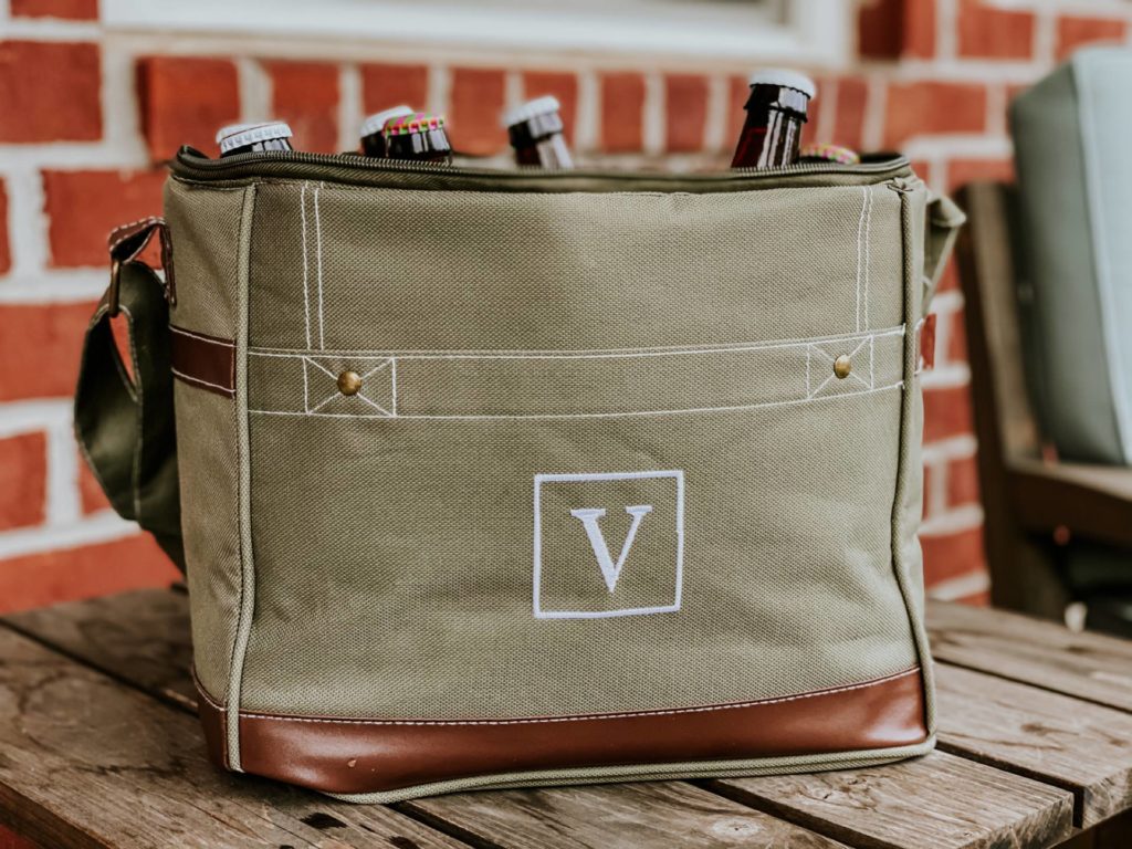 portable cooler gift with v on it filled with beers sitting on a wood table in front of red brick