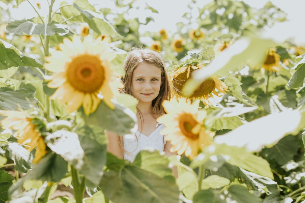 a young girl smiles betwixt sunflowers in this Tuttle Orchards Family Photo session