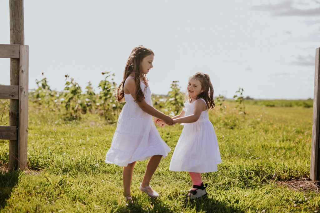 two girls in white dresses hold hands and dance in this Tuttle Orchards Family Photo session