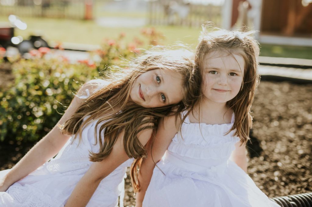 a young girl in a white dress rests her head on her younger sister's shoulder in this Tuttle Orchards Family Photo session
