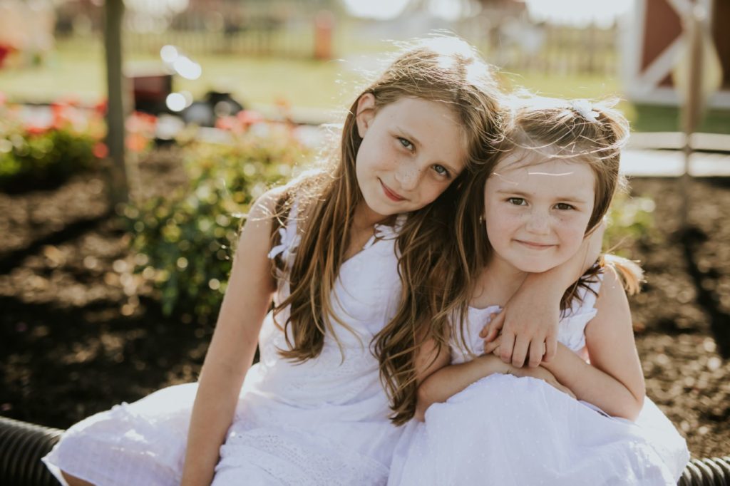 two young sisters in white dresses side hug while sitting on a bench in this Tuttle Orchards Family Photo session