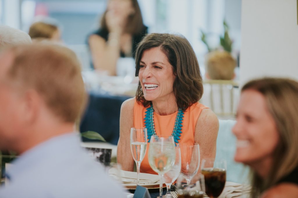 a woman in an orange dress with a turquoise necklace laughs at Conrad Indianapolis Event Photography