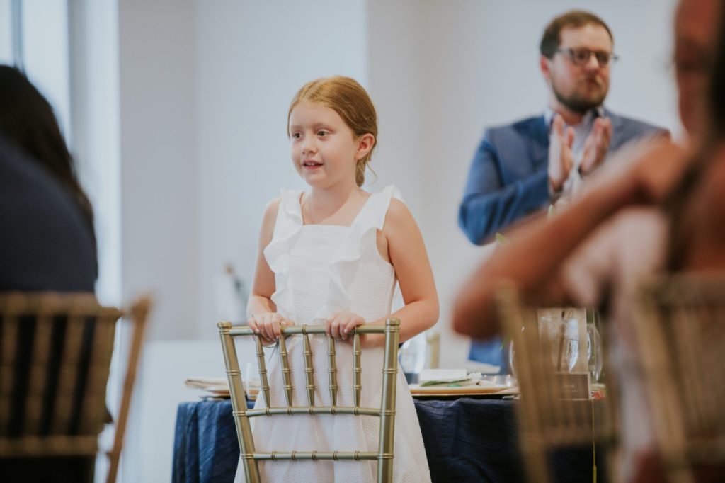 a young girl in a white dress is standing on her knees on a backwards chair at Conrad Indianapolis Event Photography