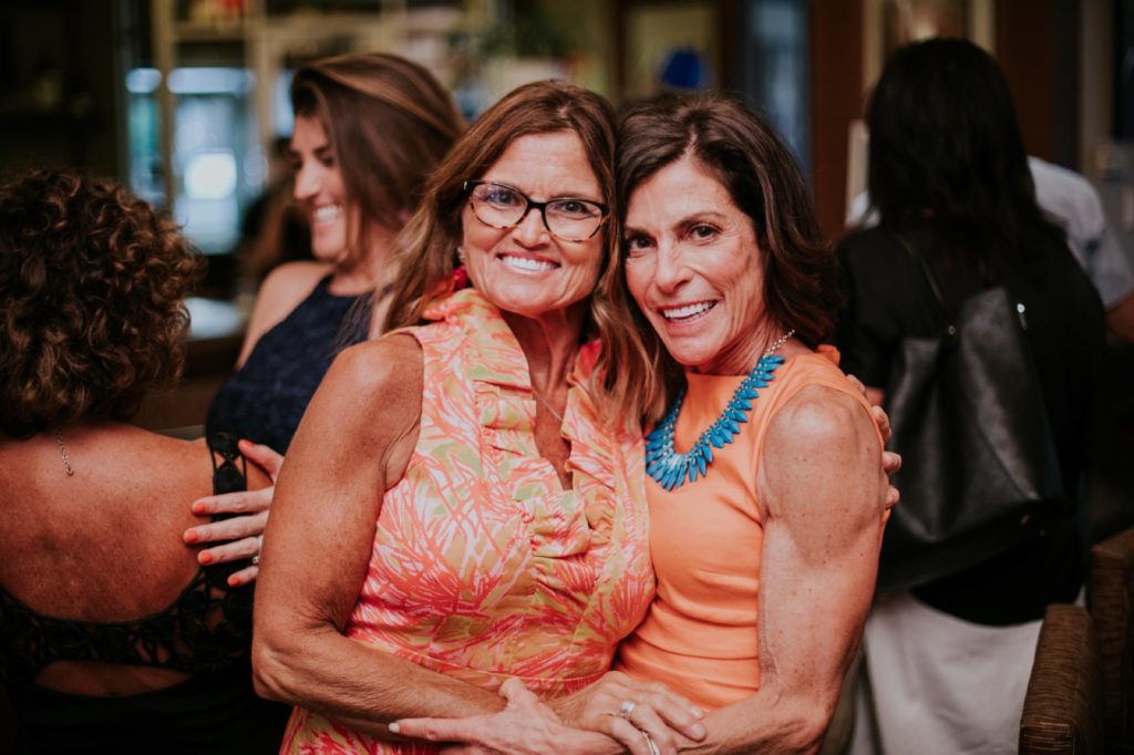two women in orange tops smile at a camera in Tastings Wine Bar and Bistro