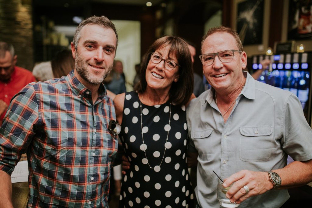 two men and one woman pose and smile for a photograph at Tastings for an event