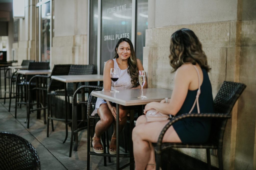 womn sit at a table outside and talk during an event at Tastings