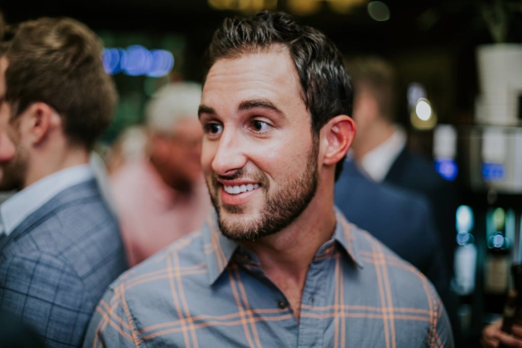 man in plaid shirt with short beard smiles in the middle of a crowed room for indianapolis event photography