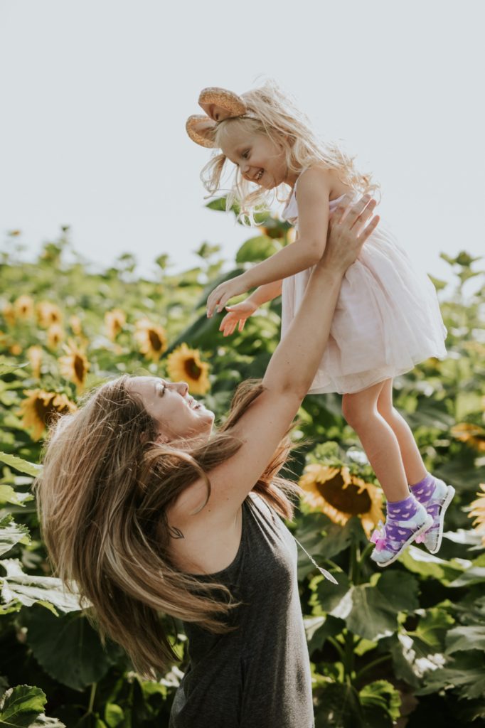 mom in green dress throws daughter into air in sunflower pictures at tuttle orchard